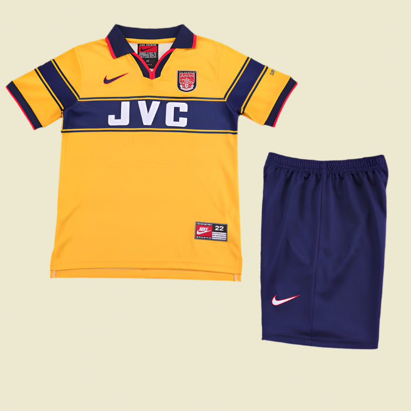 Yellow Arsenal 97-99 away kids kit with navy accents and blue shorts on a textured gray background