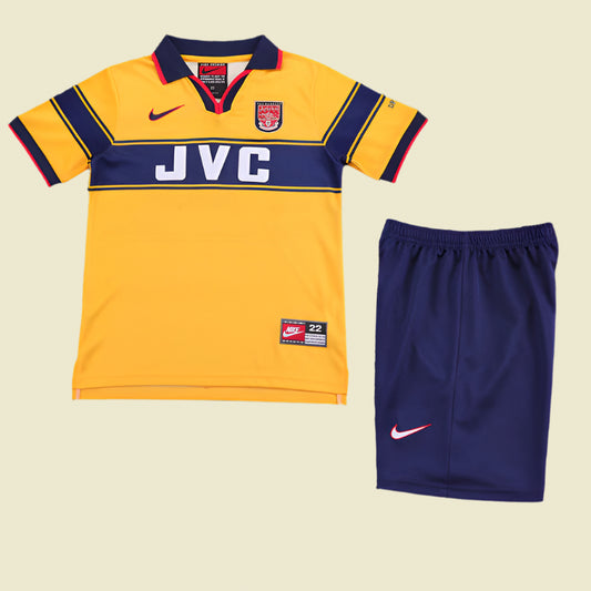 Yellow Arsenal 97-99 away kids kit with navy accents and blue shorts on a textured gray background