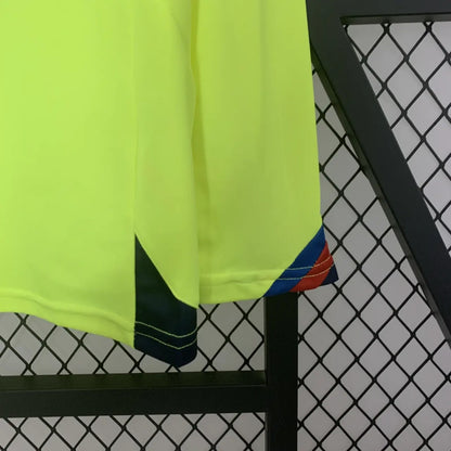 Bright yellow Barcelona 05/06 long sleeve away shirt with black and blue accents hanging on a black metal rack against a chain-link fence.