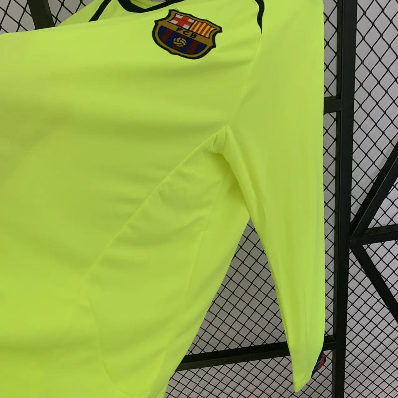 Bright yellow Barcelona 05/06 long sleeve away shirt with a logo on a black metal surface