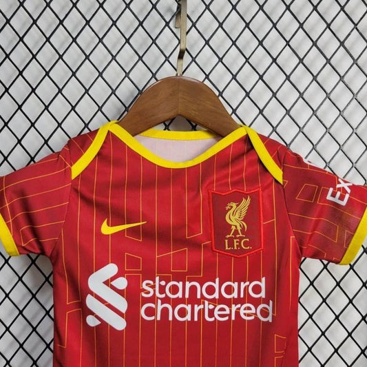Red Liverpool 24/25 home baby onesie  with yellow accents on a hanger against a wire fence background