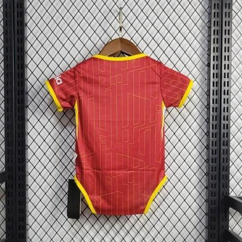 Red liverpool 24/25 home baby onesie with yellow accents hanging on a black metal rack against a tiled wall.