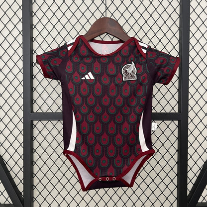 Mexico 2024 home baby onesie with red and black pattern on a hanger against a textured wall.