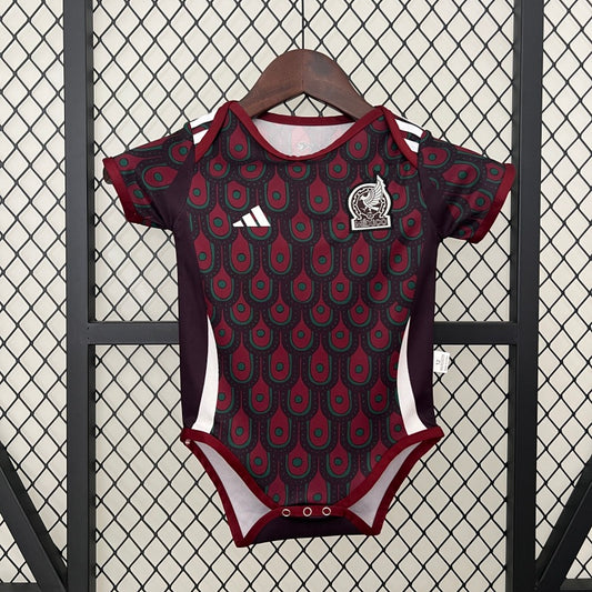 Mexico 2024 home baby onesie with red and black pattern on a hanger against a textured wall.