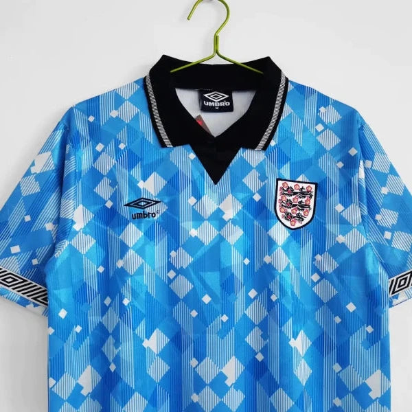 Blue England 1990 third shirt with white patterns on a hanger against a white background