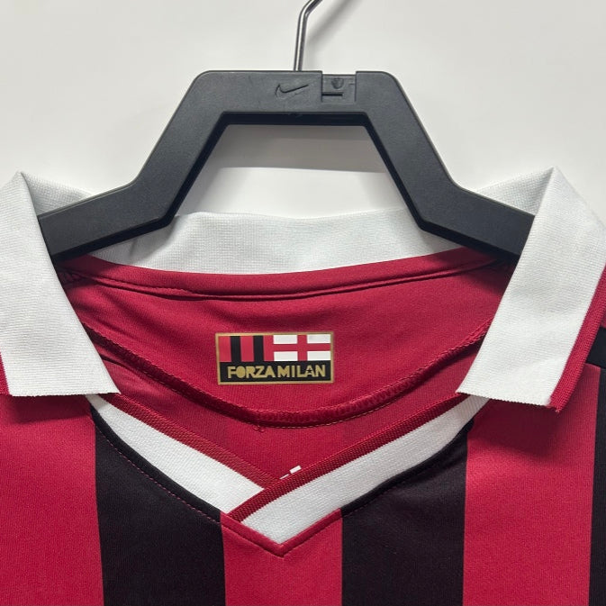 Red and black Ac Milan 09/10 long sleeve home shirt  with white collar on a hanger, featuring a brand logo.