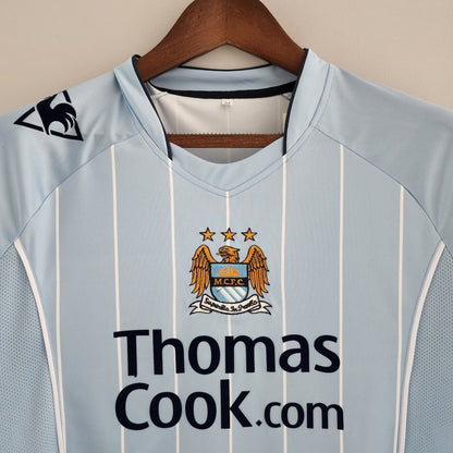 Light blue Man City 07/08 home shirt with Manchester City FC logo and 'Thomas Cook.com' text on a hanger.
