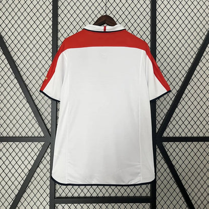 White England 2004 home shirt with red accents on a black metal stand against a wire mesh background